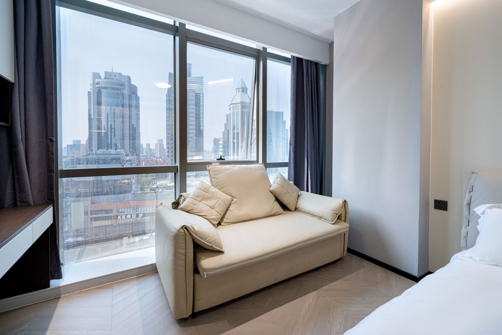 Een moderne hotelkamer met een bank, een bed en een groot raam met uitzicht op de stad.