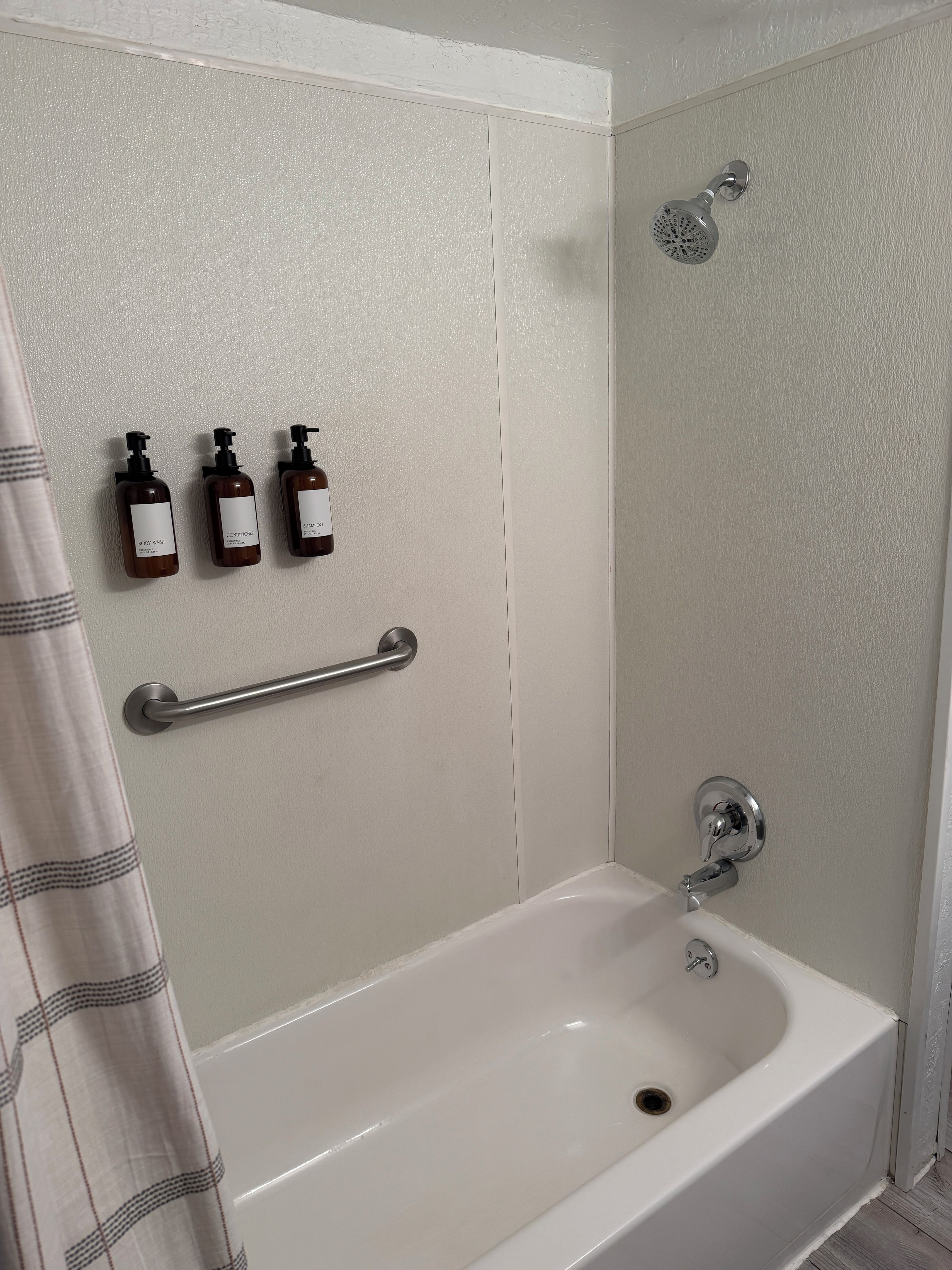 A bathroom with a bathtub, a shower, and a handrail.