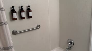 A bathroom with a bathtub, a shower, and a handrail.