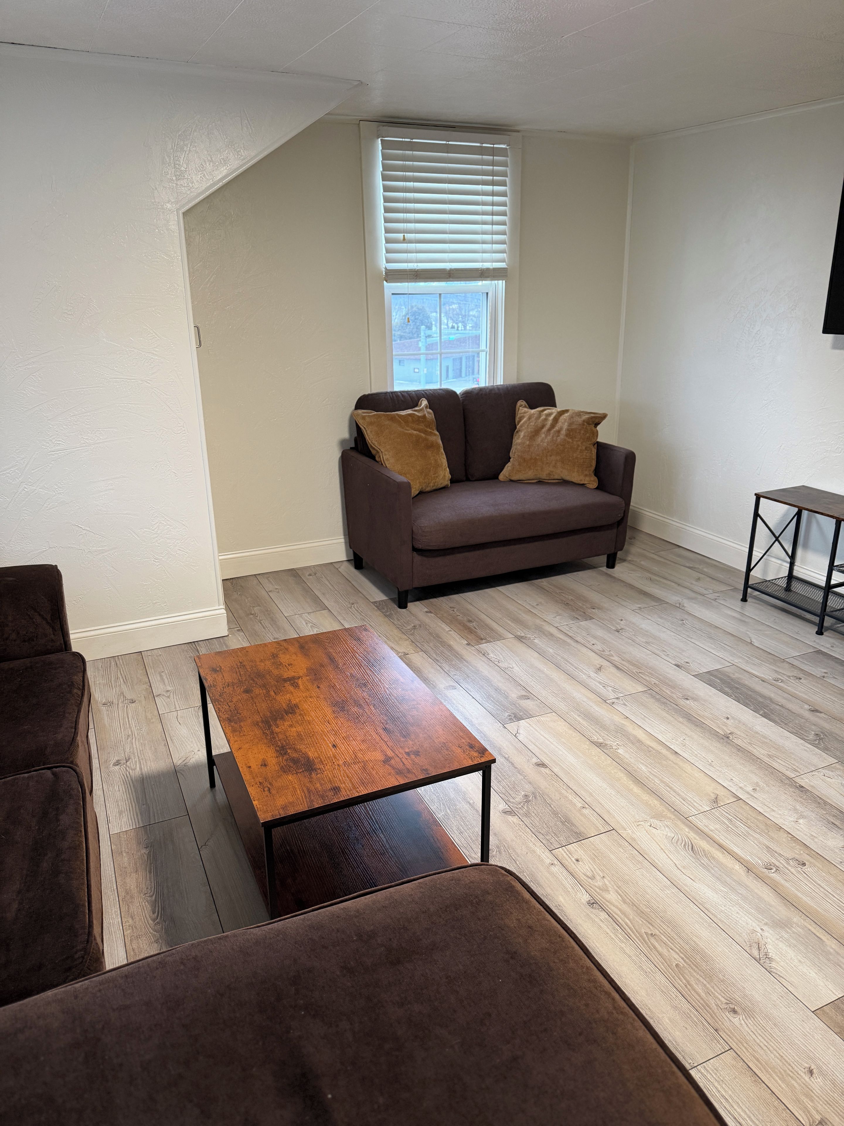 A living room with a brown sofa, a wooden coffee table, and a window with blinds.