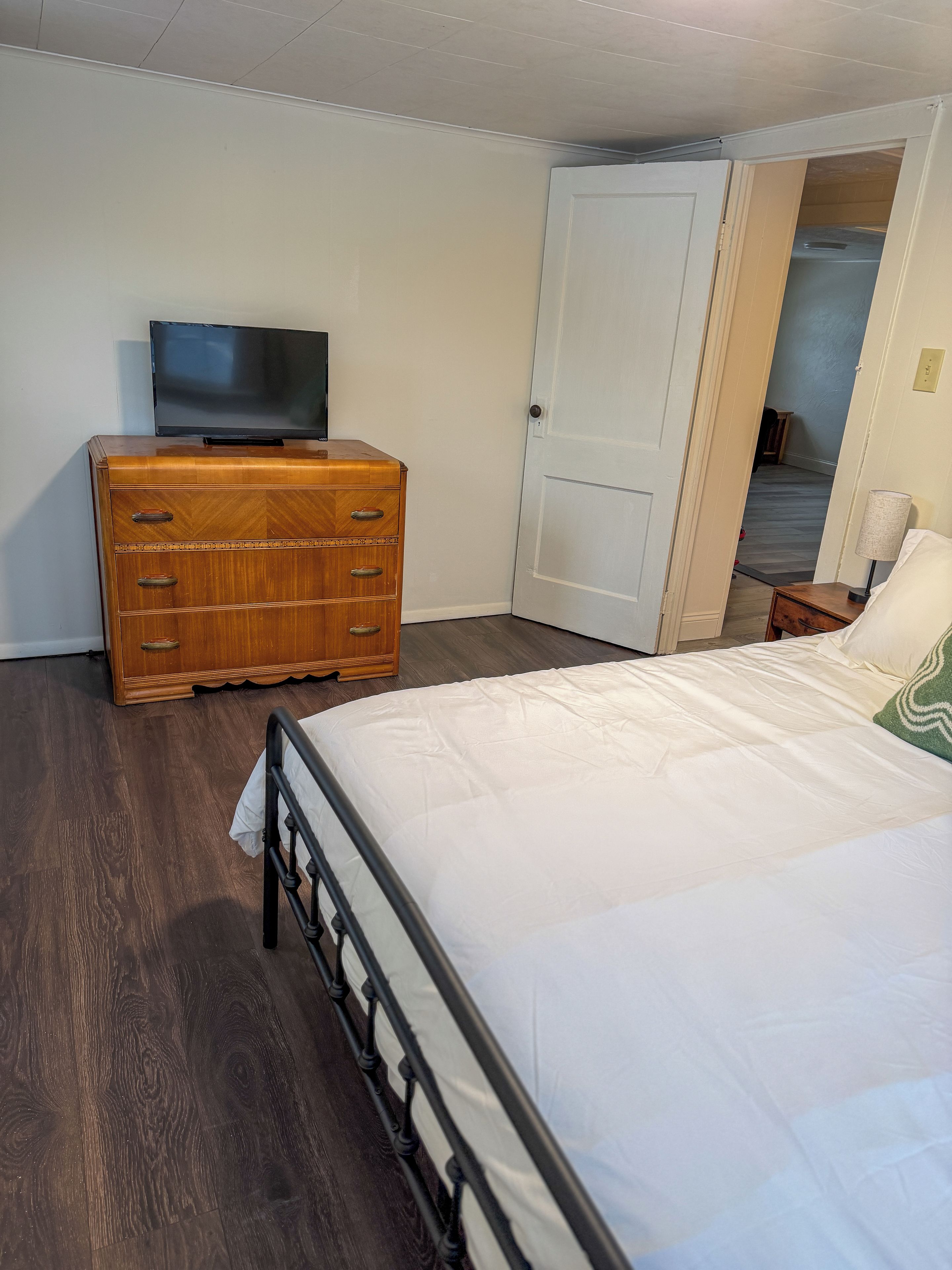 A bedroom with a bed, dresser, television, and a door leading to another room.