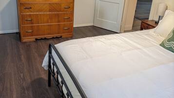 A bedroom with a bed, dresser, television, and a door leading to another room.