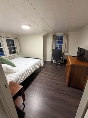 A bedroom with a bed, a desk, a chair, and a television.