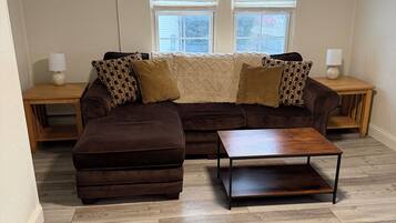 A living room with a brown sectional sofa, an ottoman, a wooden coffee table, and two nightstands with lamps.