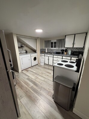 A compact kitchen with a washing machine, a stove, and a trash bin.