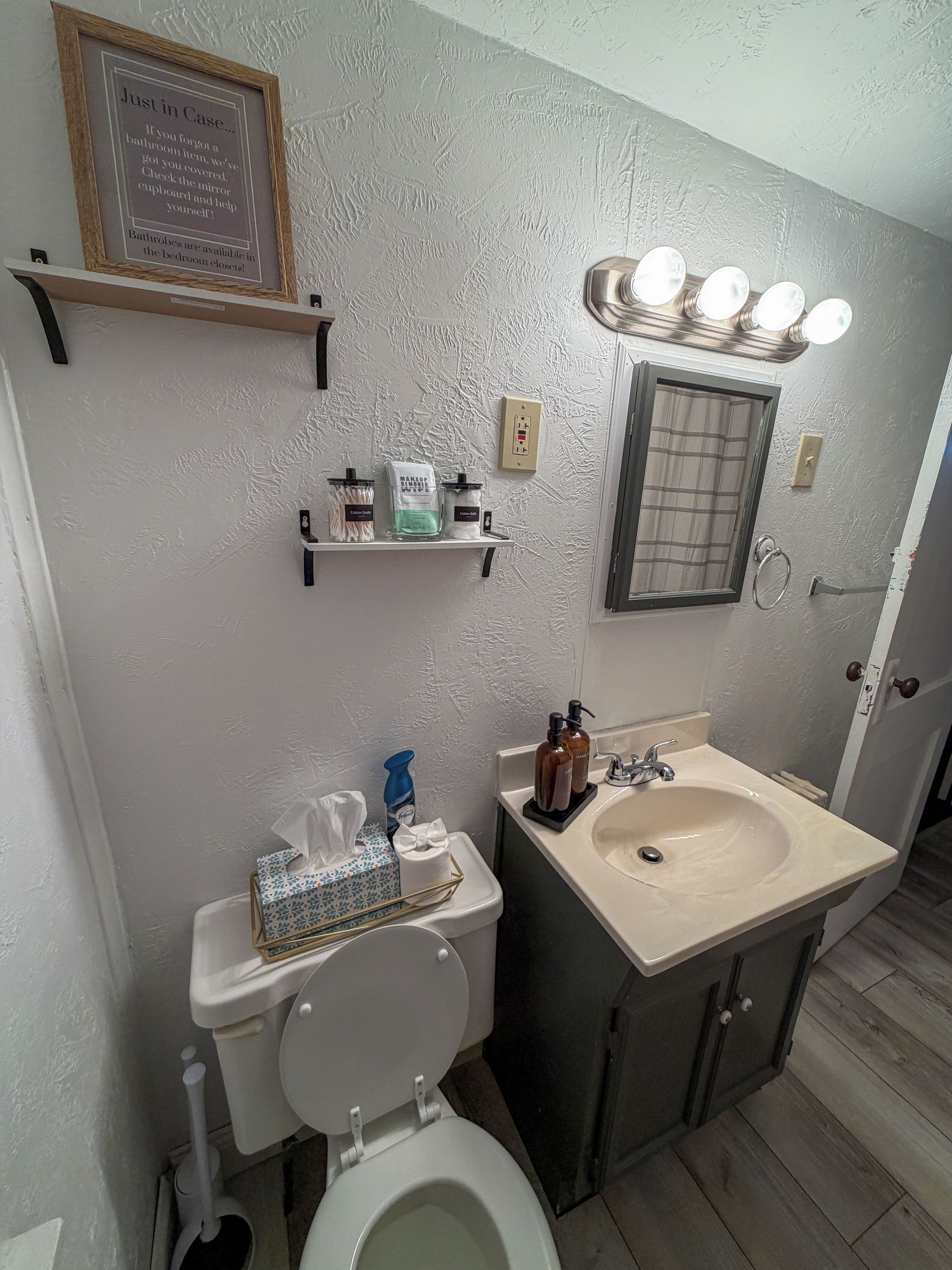 A bathroom with a toilet, sink, and shelves with toiletries.