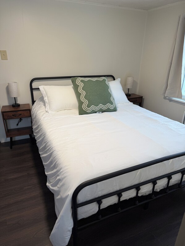 A bed with white bedding, a green pillow with a white border, and two bedside tables with lamps.