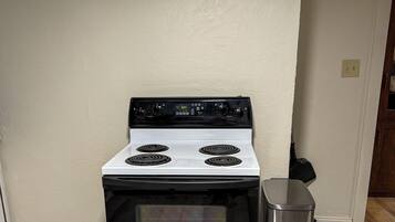 A kitchen with a white stove, a stainless steel trash can, and wooden flooring.