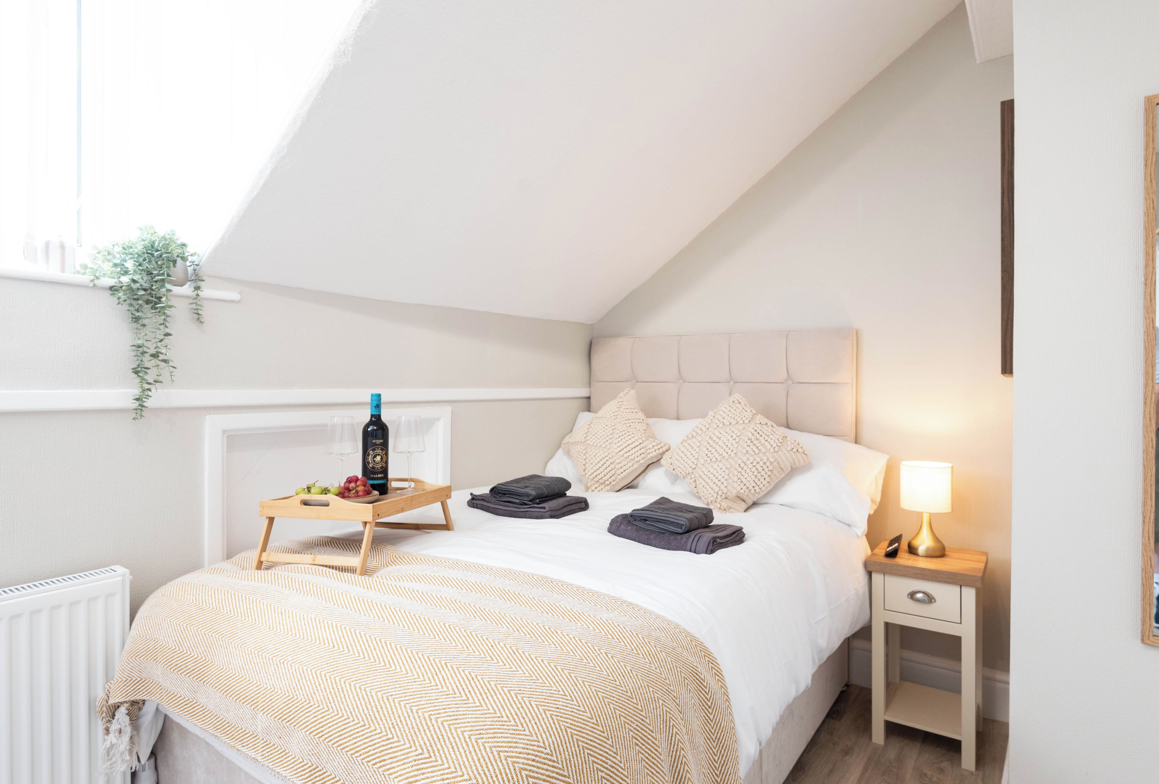 Ein Schlafzimmer mit einem Bett, Nachttischen, einem Heizkörper und einem Fenster mit einer Pflanze.