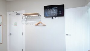 Ein Zimmer mit einer weißen Tür, einem Kleiderständer, einem an der Wand befestigten Fernseher, der ein Sprachauswahlmenü anzeigt, und einem kleinen Schild mit Notfallhinweisen.
