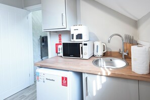 Una kitchenette compacta con microondas, tostadora y refrigerador pequeño.