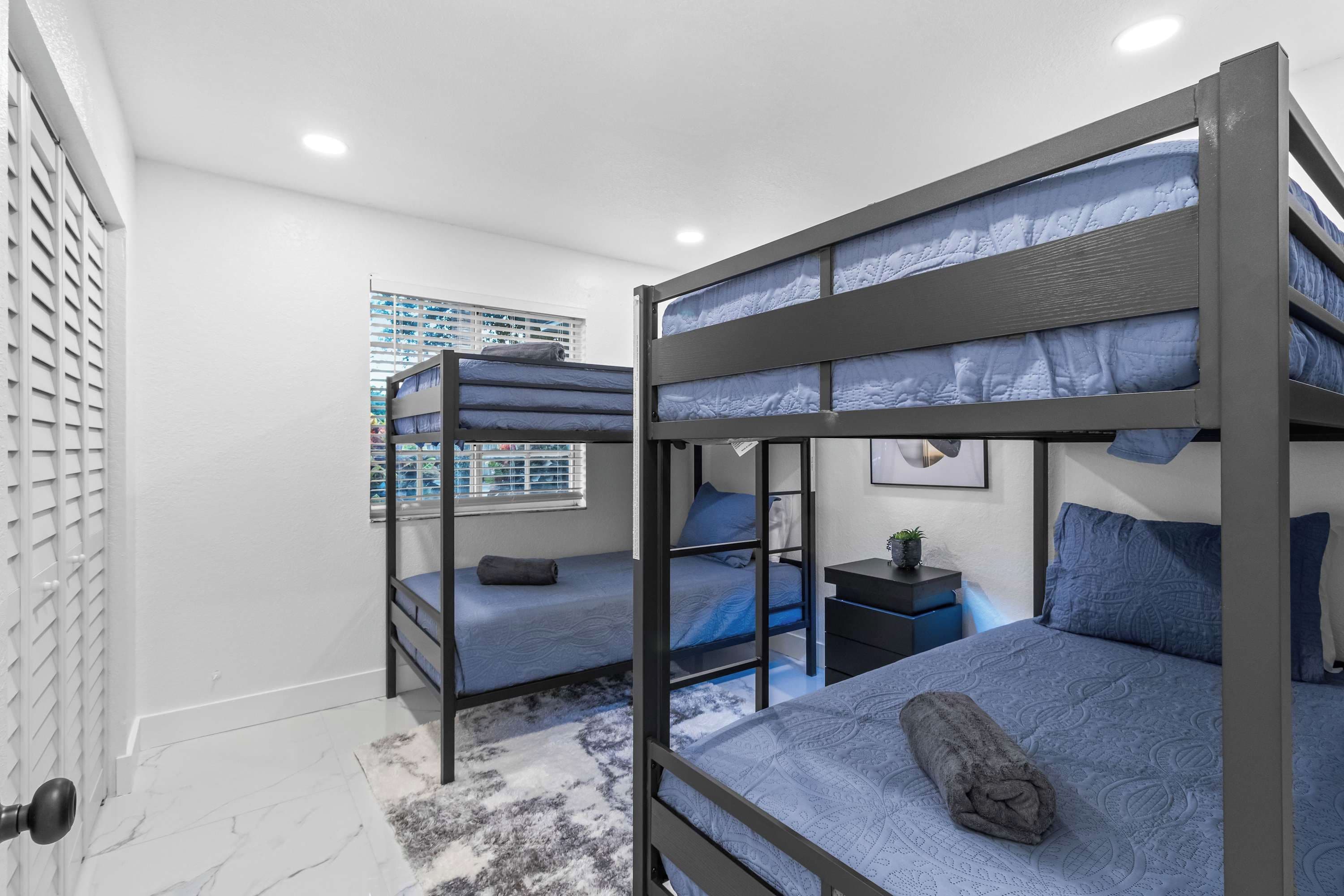 A bunk bed room with a window, a small bedside table, and a rug.