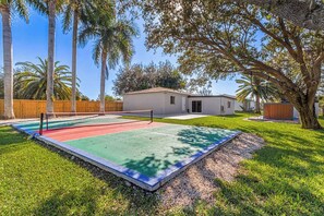 Ein Wohnhaus mit Tennisplatz, einem kleinen Haus und einem eingezäunten Garten.