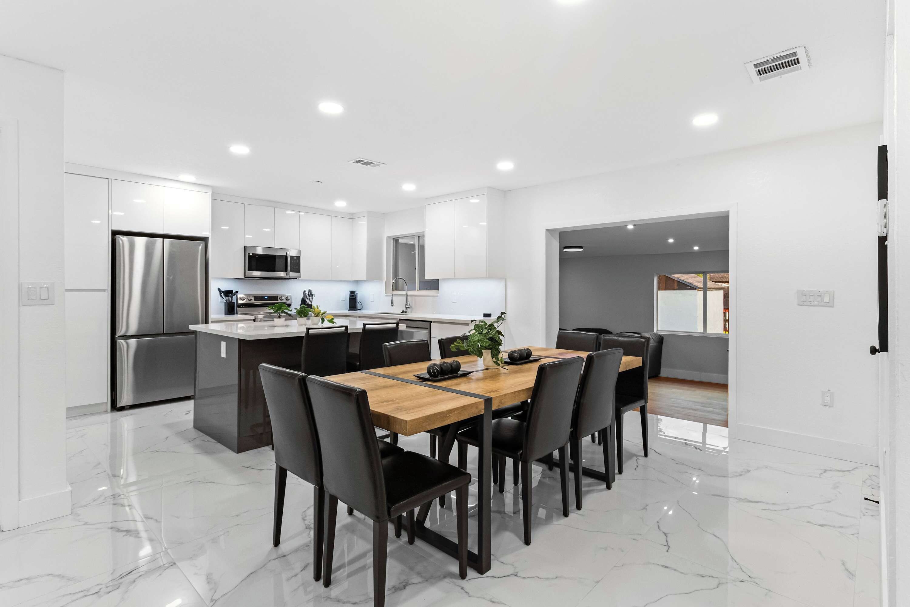 A modern kitchen with stainless steel appliances, a dining area with a marble floor, and a view into the living area.