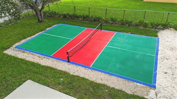 Ein Tennisplatz mit Netz, umgeben von Rasen und einer Sandfläche.