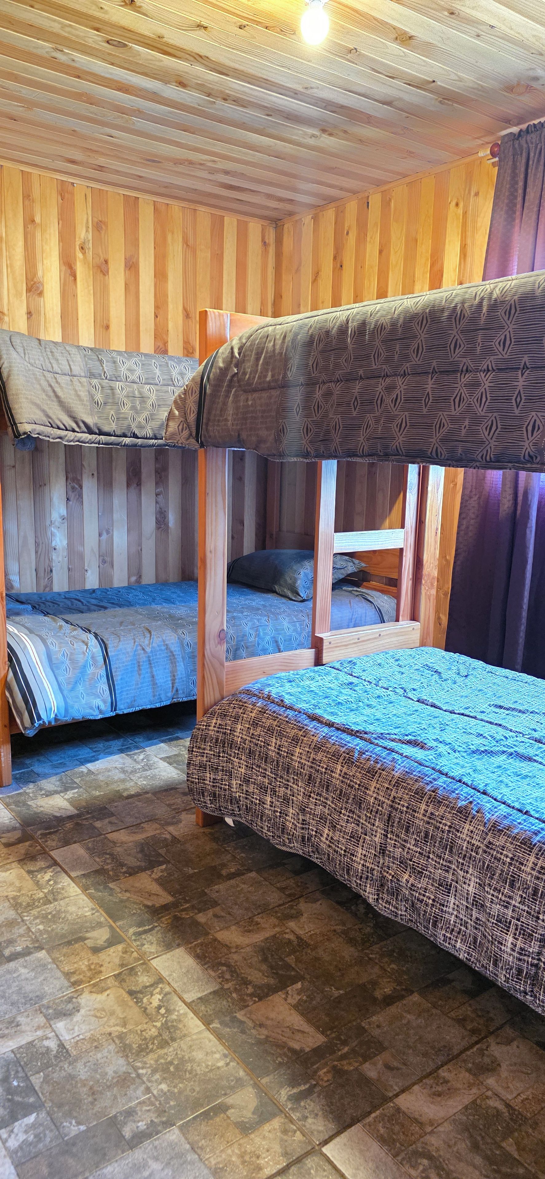 A room with two bunk beds, wooden walls, and a tiled floor.