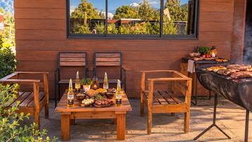 An outdoor dining area with a wooden table set for a meal, two chairs, and a grill.