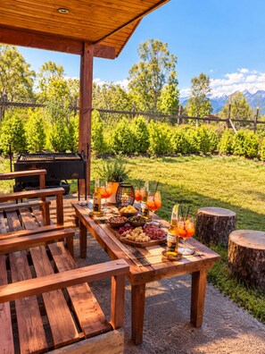 An outdoor patio with wooden tables and benches, a barbecue grill, and a view of a mountainous landscape. - Cabañas don Agustín Pucón  (Pucón)