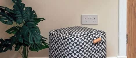 Una habitación con un espejo redondo en la pared, una planta en maceta y un otoman con estampado.