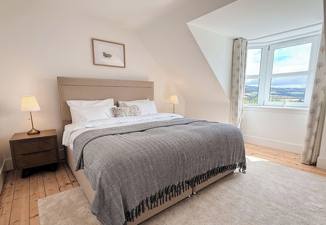 A bedroom with a bed, nightstands, a window with a view, and a framed picture on the wall.