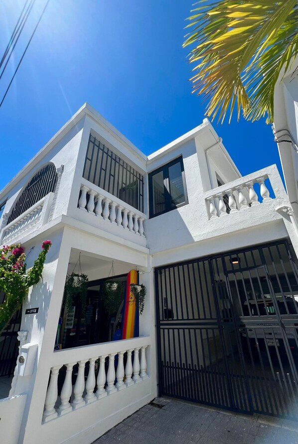 Un edificio de dos pisos con fachada blanca, ventanas grandes y un portón negro.
