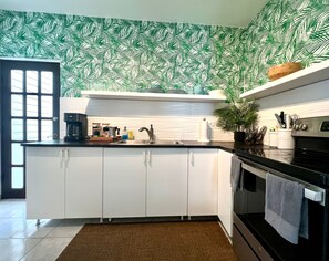 Una cocina moderna con armarios blancos, encimera negra y salpicadero con estampado de hojas verdes.