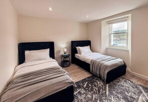 A hotel room with two beds, a small table, and a window with a view. - Harbour View Stonehaven (Aberdeenshire)