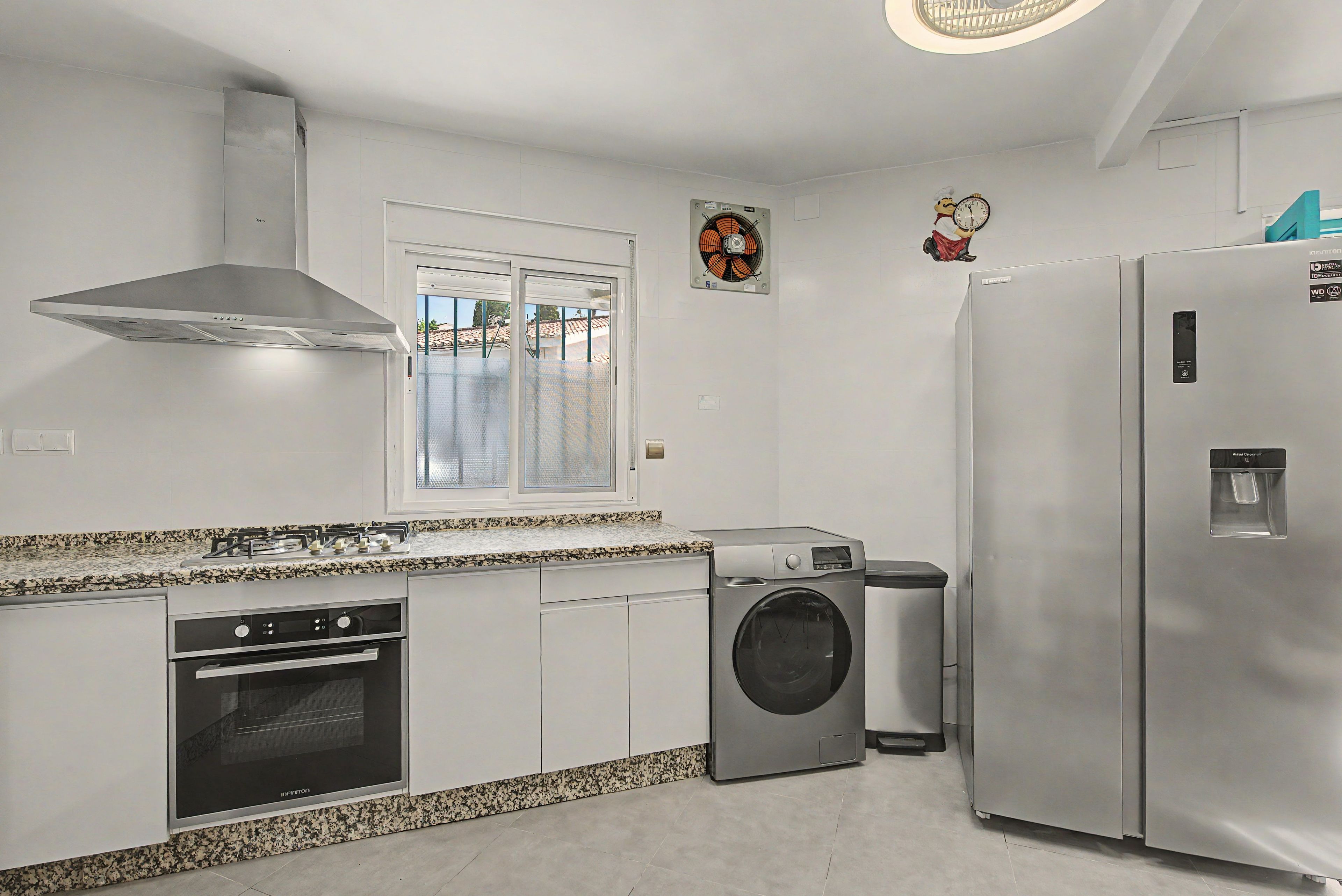 Una cocina moderna con electrodomésticos de acero inoxidable, horno empotrado, lavadora y refrigerador.