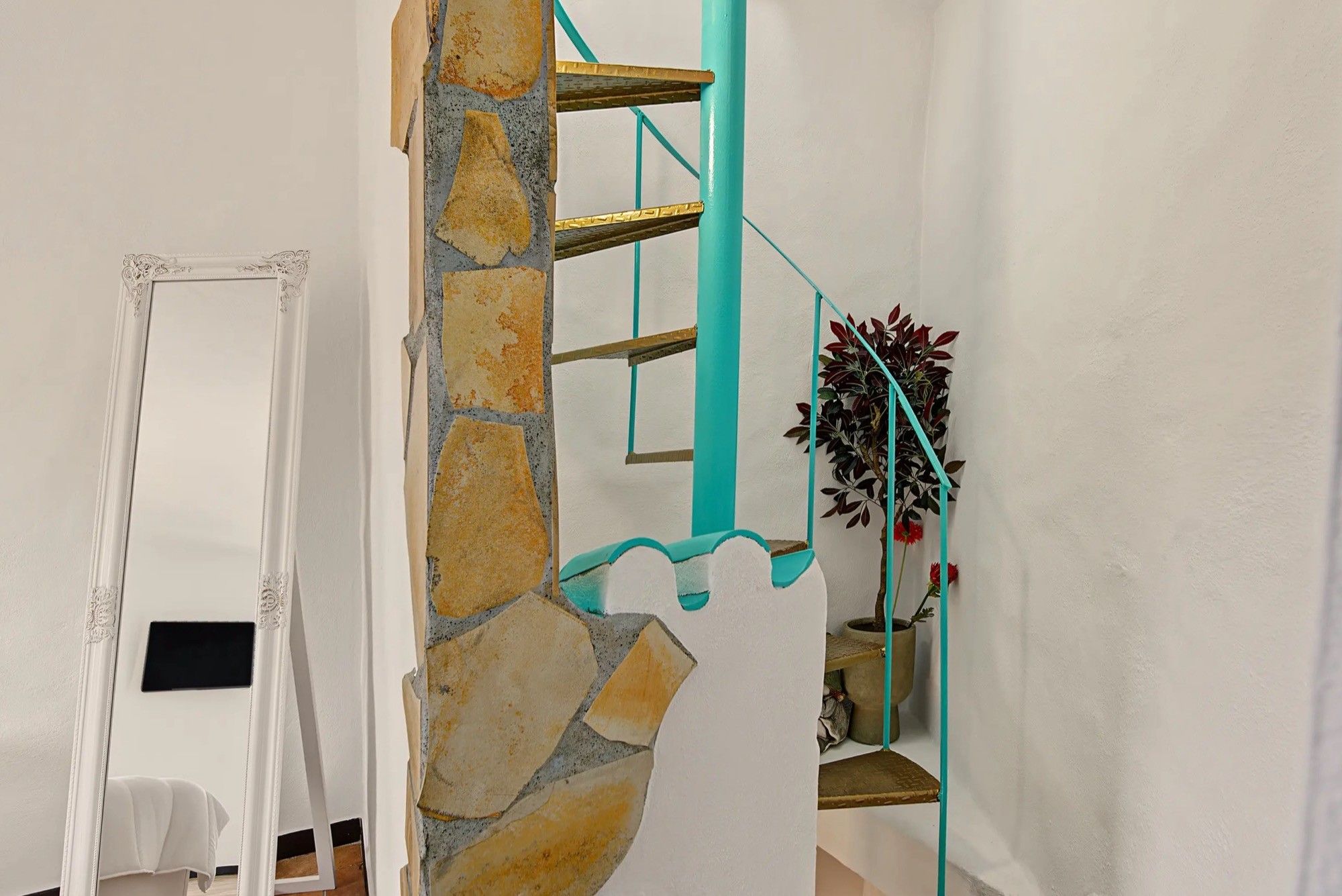Eine Treppe mit einer Steinsäule, einem türkisblauen Geländer und einem Blumentopf.