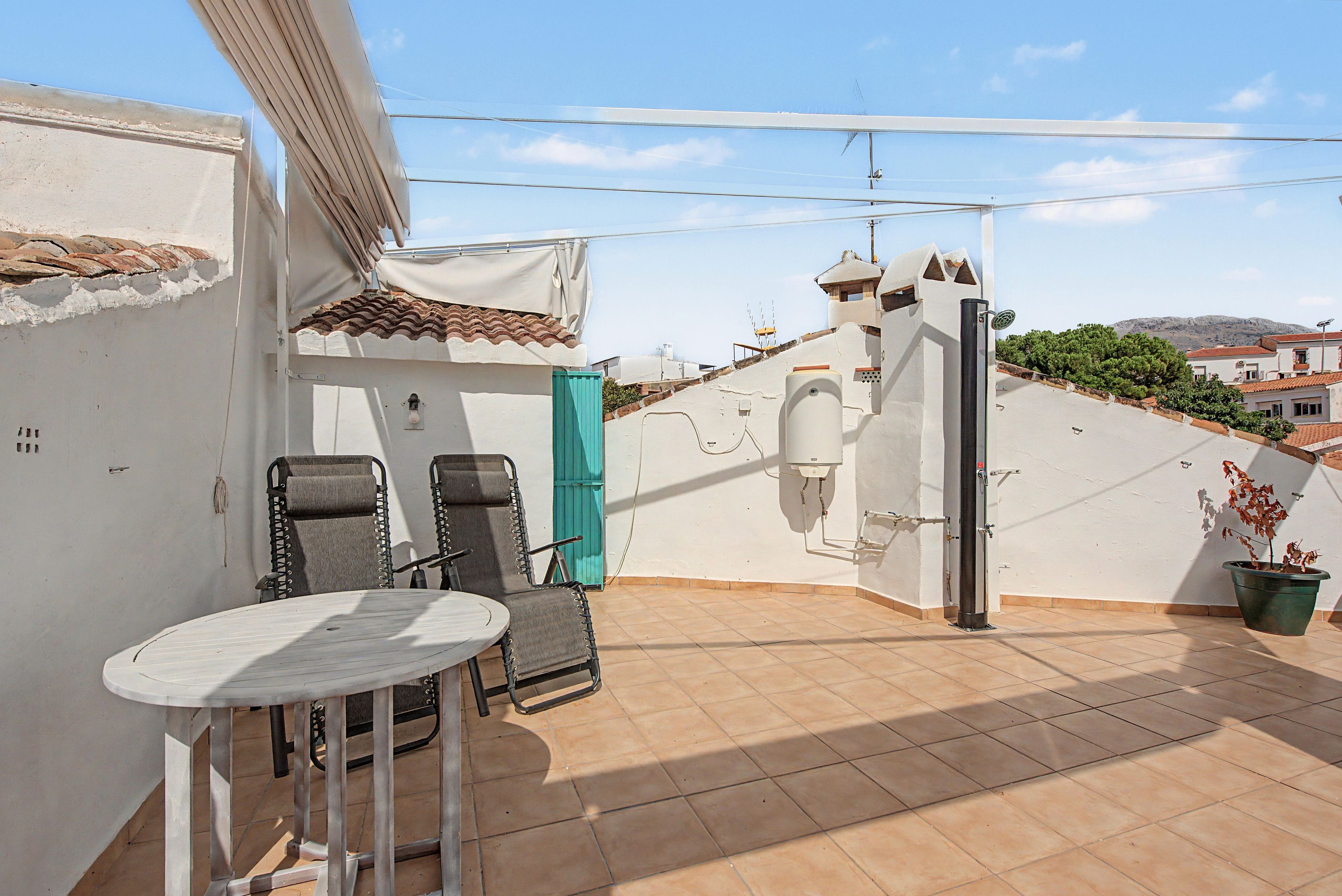 Eine Dachterrasse mit Tisch und Stühlen, einem Blumentopf und einem Warmwasserbereiter.