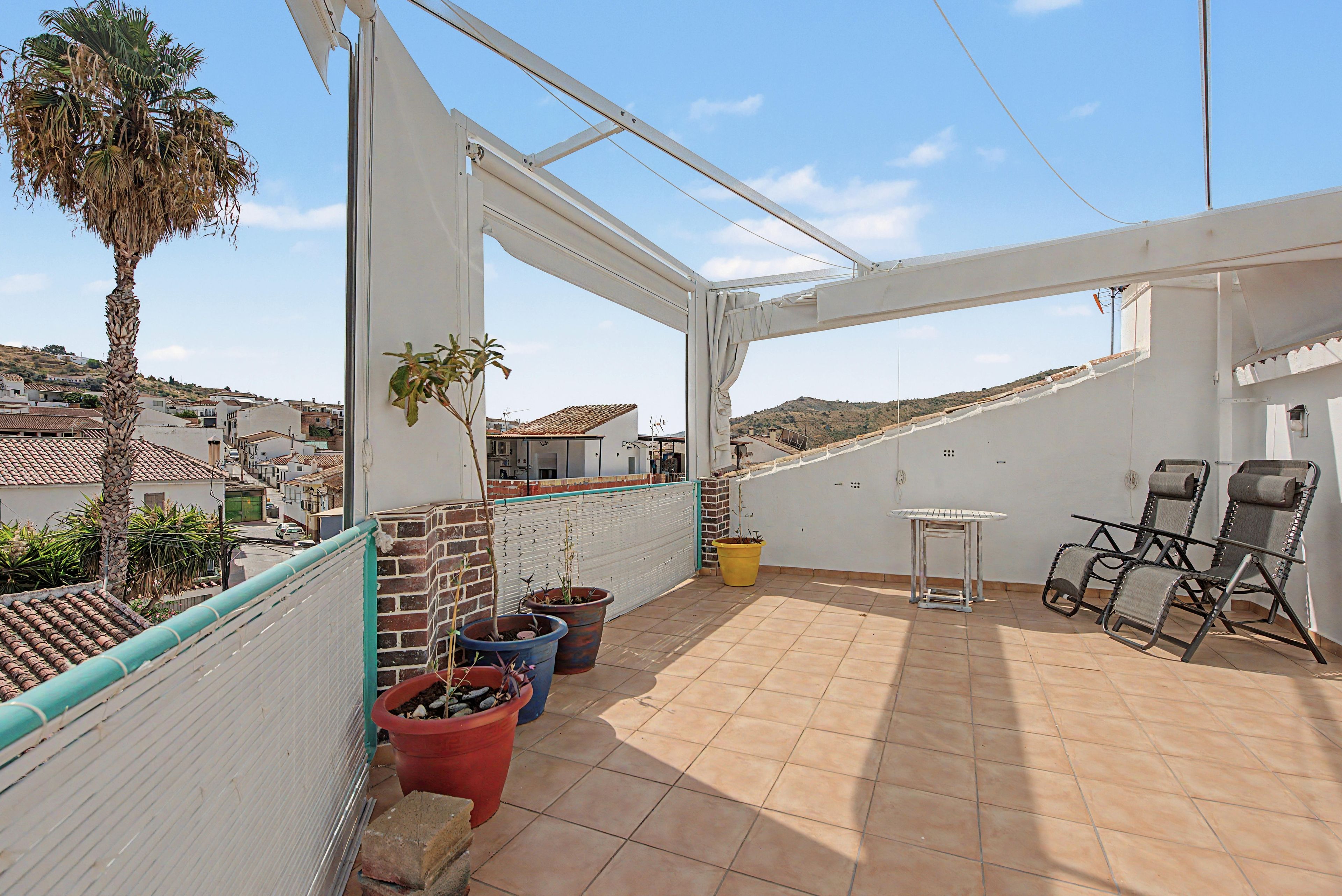 Una terrazza sul tetto con pavimento piastrellato, piante in vaso, un tavolo e due sedie.