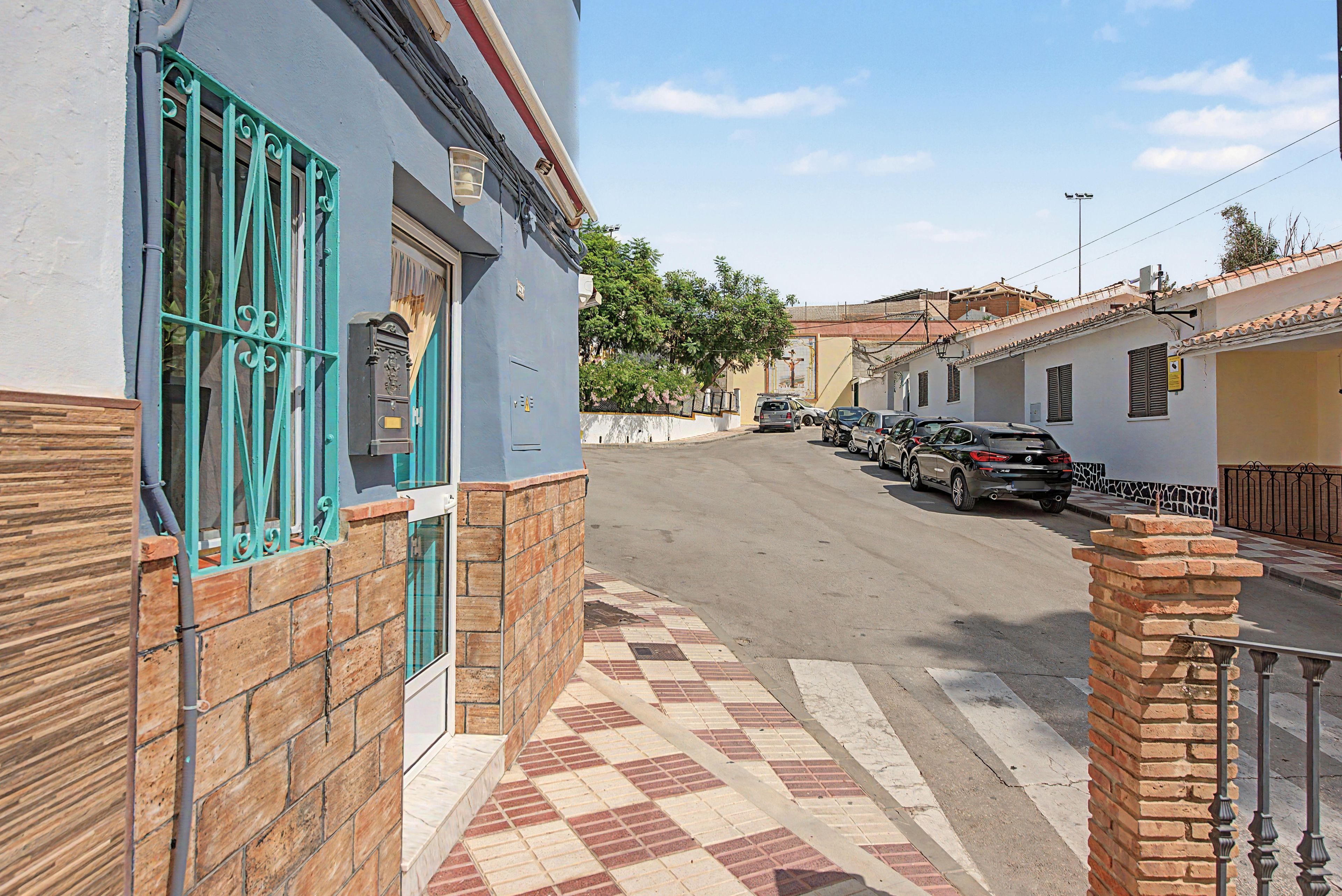 Una vista di una strada con auto parcheggiate, un edificio con facciata blu e un marciapiede in lastre.