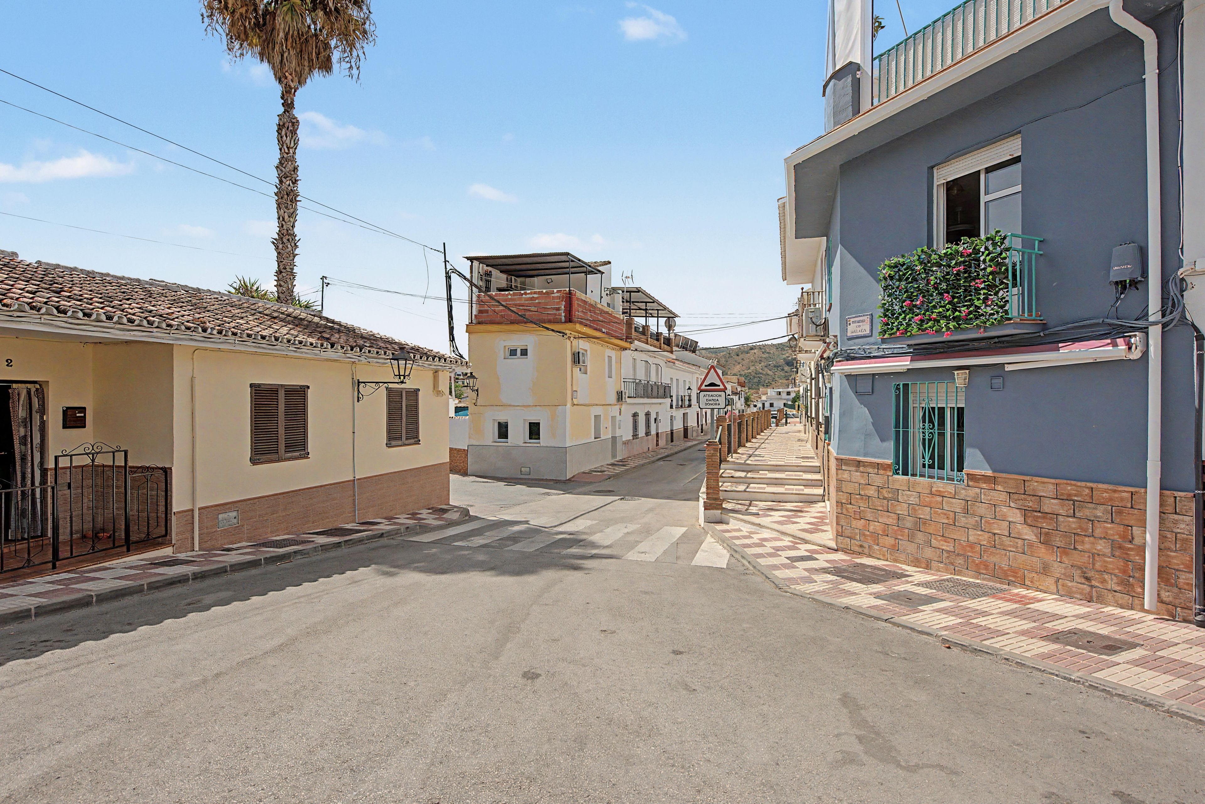 Vista de la calle con edificios, una palmera y cielo despejado.