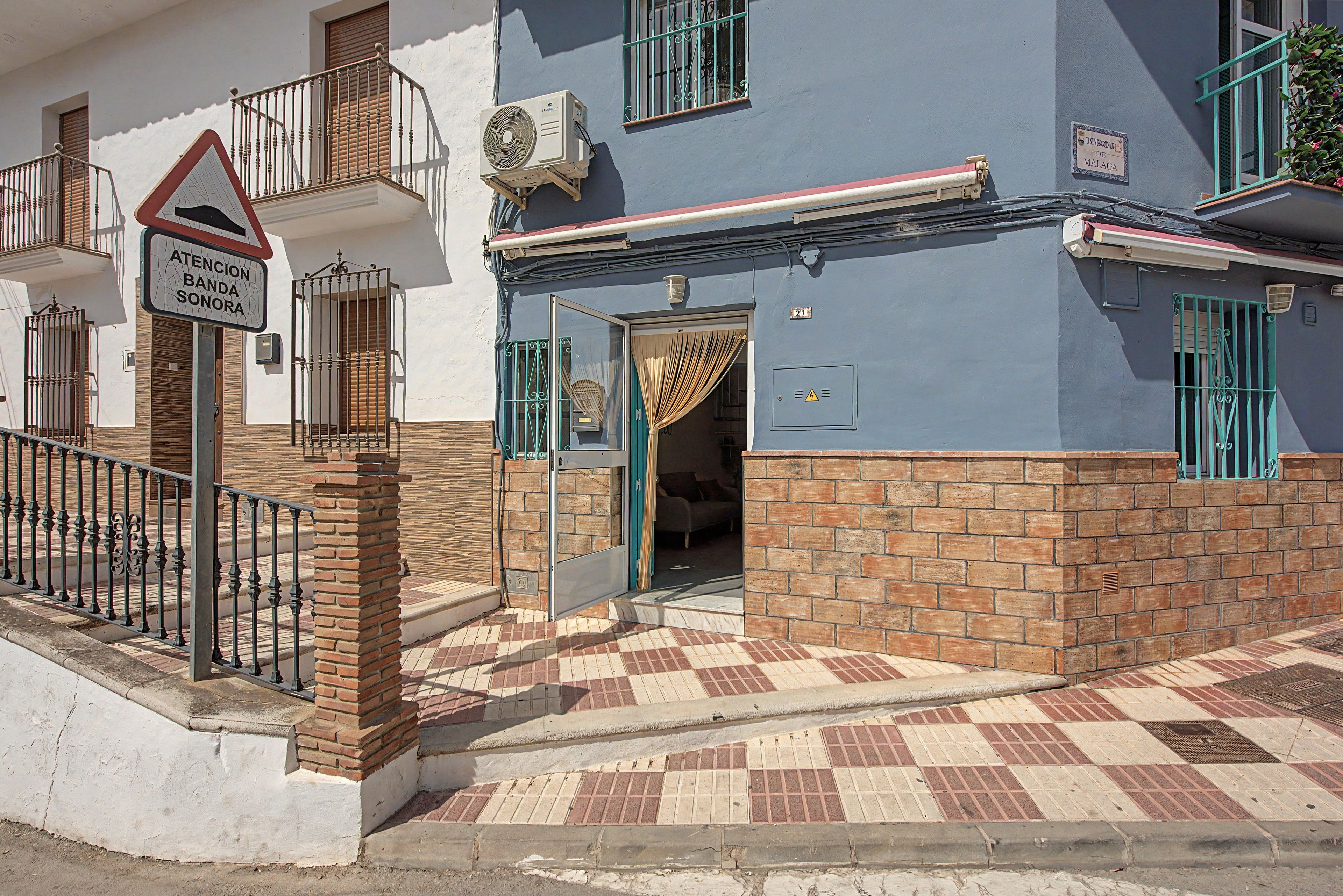 Un edificio con base de ladrillo y sección superior azul, entrada con portón y un letrero que indica un espacio para ensayos de banda.