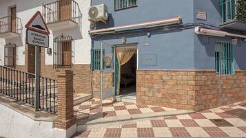 Un edificio con base de ladrillo y sección superior azul, entrada con portón y un letrero que indica un espacio para ensayos de banda.