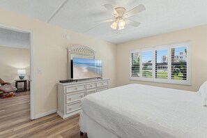 A bedroom with a bed, a television, a dresser, a ceiling fan, and a window with blinds. - Ocean Terrace Club 107 (Port Orange)