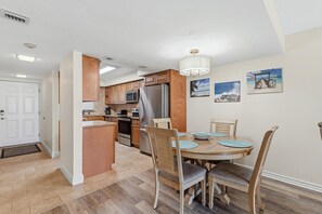 A modern kitchen with wooden cabinets, stainless steel appliances, and a dining area with a table and chairs. - Ocean Terrace Club 107 (Port Orange)