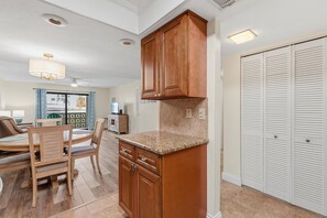 A kitchen with wooden cabinets, a granite countertop, and a dining area with a table and chairs. - Ocean Terrace Club 107 (Port Orange)