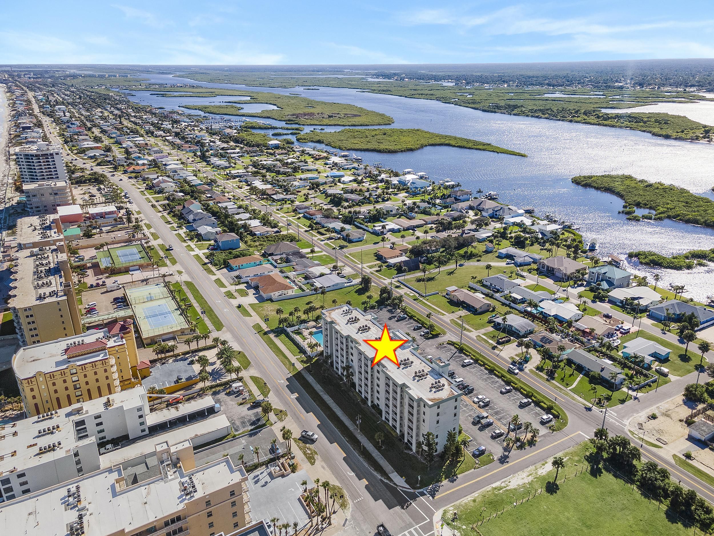 Une vue aérienne d’un quartier résidentiel situé sur la côte, avec un hôtel imposant doté d’une piscine sur le toit et d’un grand symbole en forme d’étoile.