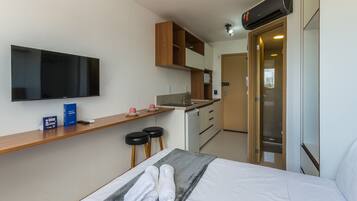A compact hotel room with a bed, a TV, a kitchenette, and a bathroom.