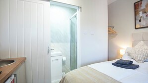 Ein Hotelzimmer mit Bett, Nachttisch, Spiegel, Kleiderschrank und einer Duschkabine.