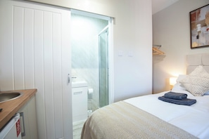 Ett hotellrum med en säng, ett sängbord, en spegel, en garderob och en duschhörna.