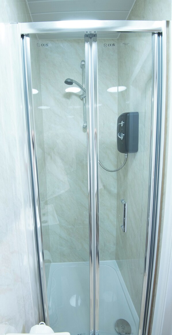 A glass-enclosed shower stall with a handheld showerhead and a wall-mounted control panel.