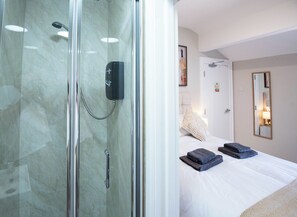 A hotel room with a glass-enclosed shower, a bed with neatly folded towels, and a bedside lamp.