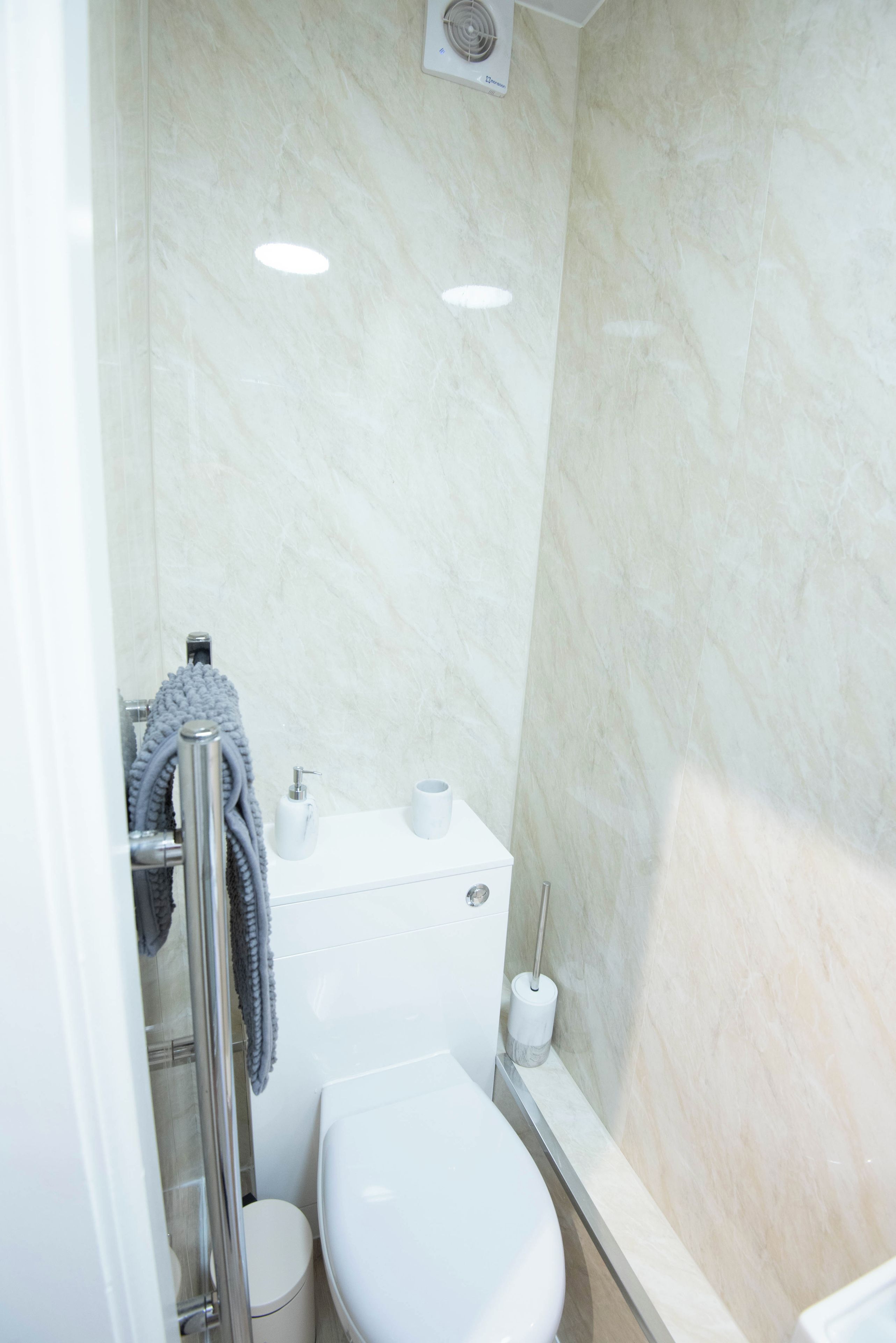 A bathroom with a toilet, a hand dryer, a towel rack, and a shower area.