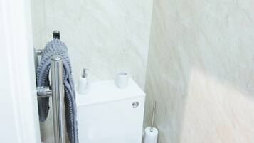 A bathroom with a toilet, a hand dryer, a towel rack, and a shower area.