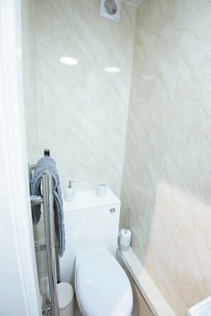 A bathroom with a toilet, a hand dryer, a towel rack, and a shower area.
