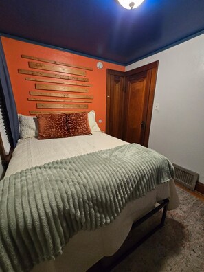 Ein Schlafzimmer mit Bett, Holz-Kopfteil, einer Tür und einem Heizkörper.