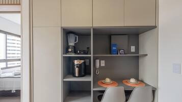 A compact kitchenette with a coffee maker, a blender, a phone, and a small table with chairs.