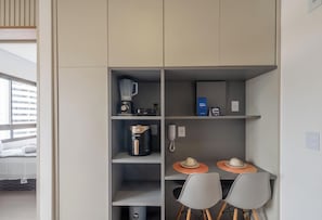 Eine kleine Küchenzeile mit Kaffeemaschine, Mixer, Telefon und einem Tisch mit Stühlen.